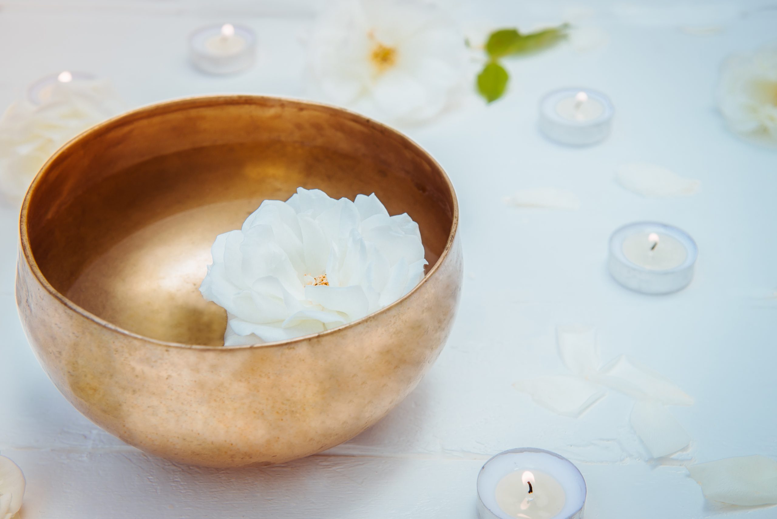 Close up Tibetan singing bowl with floating in water rose inside. Burning candles, flowers petals on the white wooden background. Meditation and Relax. Exotic massage. Copy space